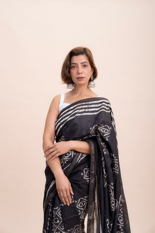 A woman in pure black cotton saree with a white geometric batik print and zari woven border featuring tassels.