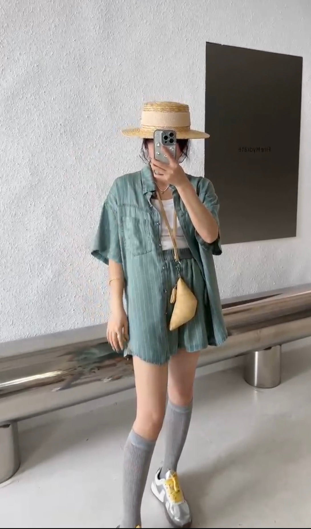 A woman wearing an oversized denim shirt with long sleeves and a collared neck, paired with denim shorts, standing indoors.