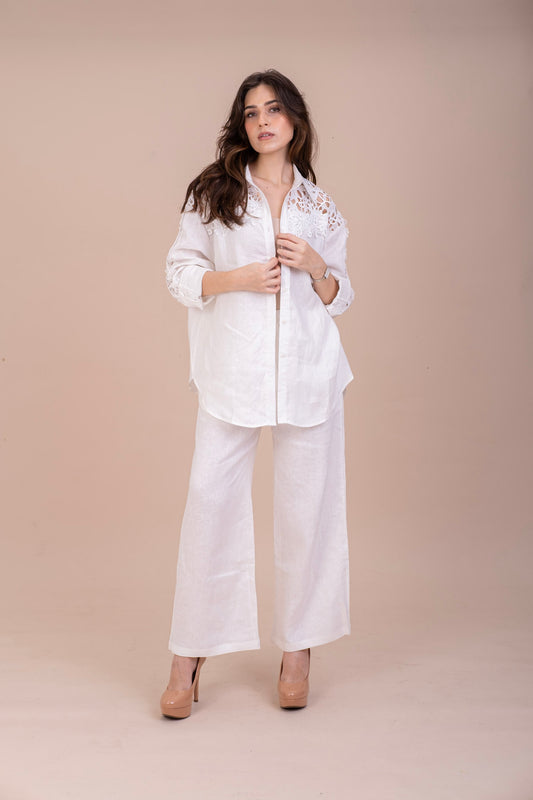 woman in white oversized pure linen button up shirt with lace cut out detailing on the shoulders, full sleeves shirt paired with linen white pants