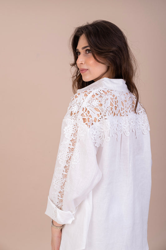 A woman in a white pure linen oversized shirt with floral lace detailing on the sleeves and shoulder, viewed from the back.