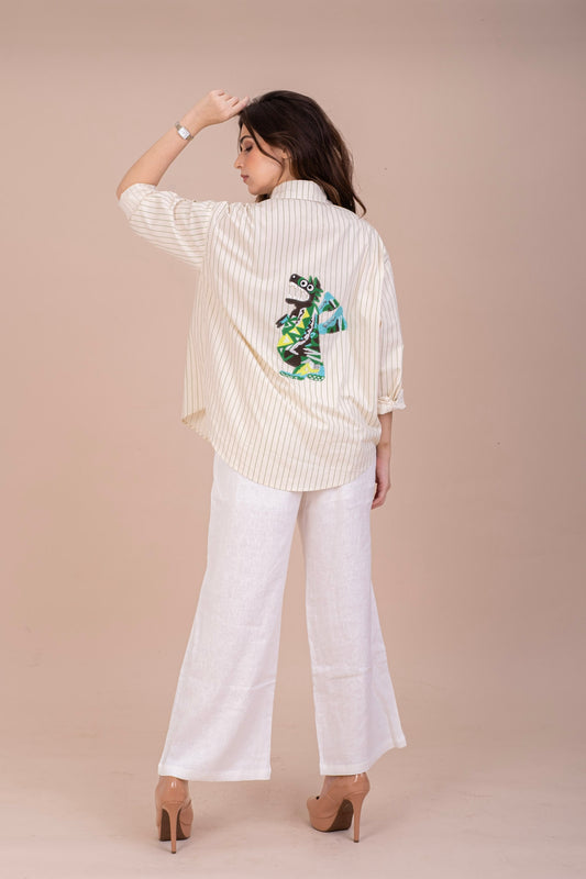 A woman wearing a off white button-up cotton shirt with green pinstripes and a unique embroidered design on the back