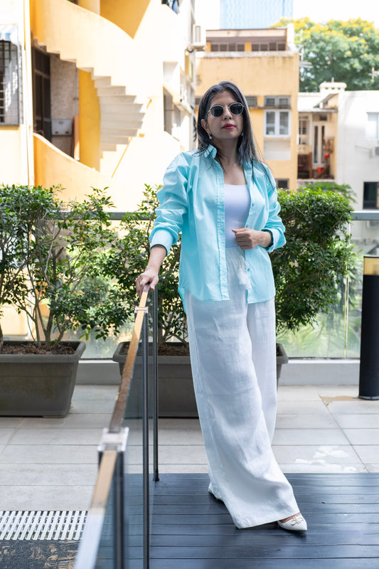 Woman wearing a pastel blue relaxed fit cotton button up shirt with white linen pants