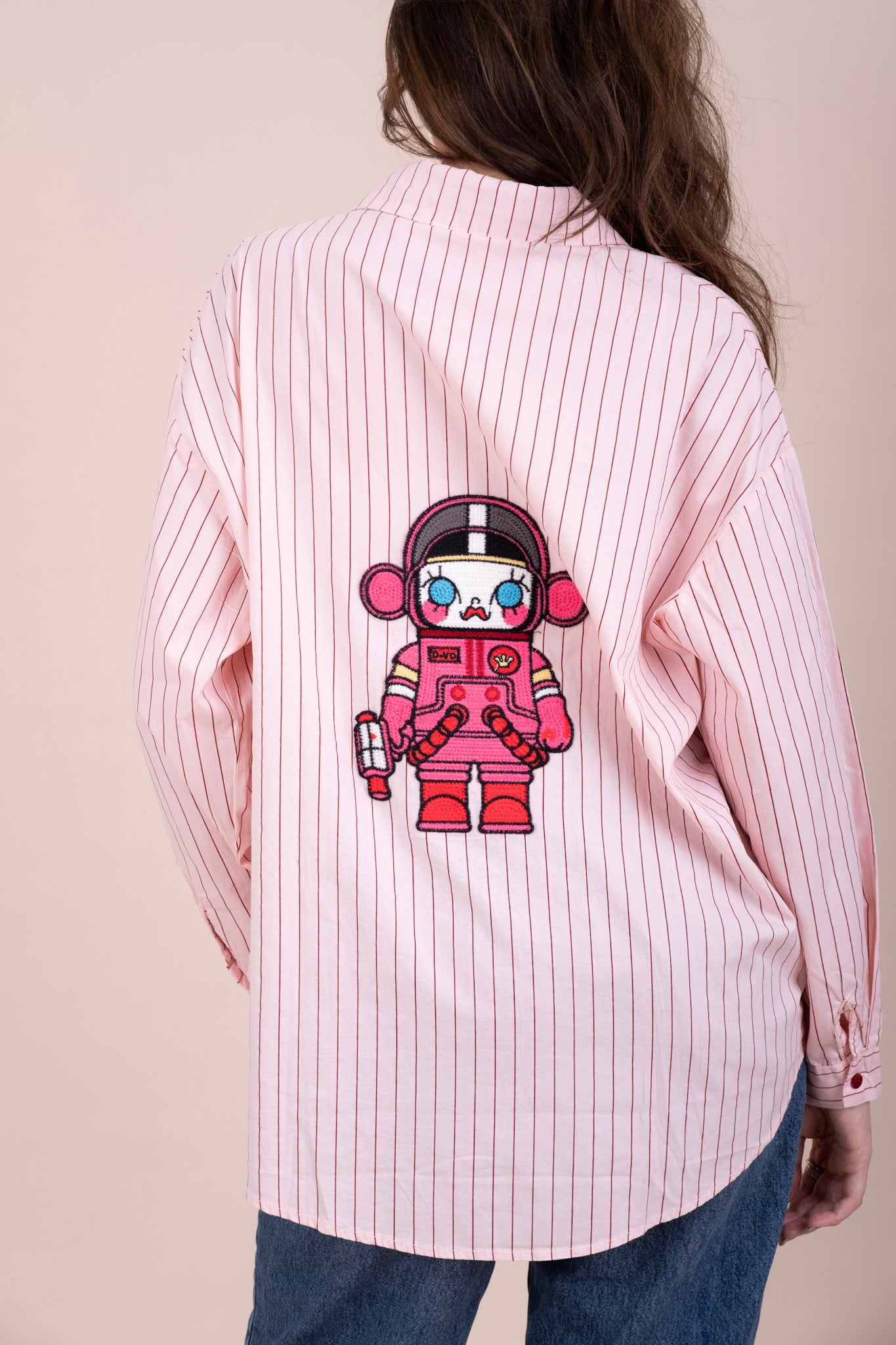 A woman viewed from the back wearing a pink and white vertically striped button-up shirt with a large cartoon astronaut graphic printed on the back
