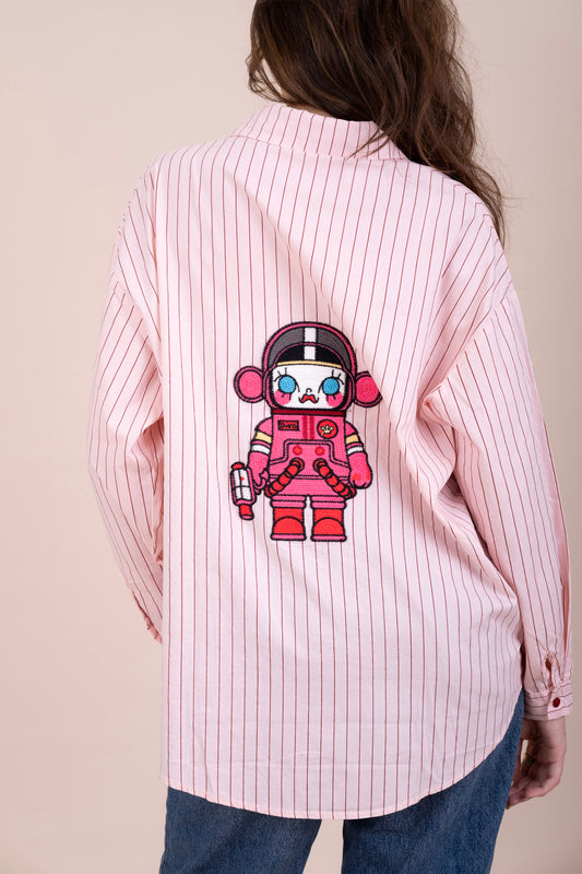 A woman viewed from the back wearing a pink and white vertically striped button-up shirt with a large cartoon astronaut graphic printed on the back
