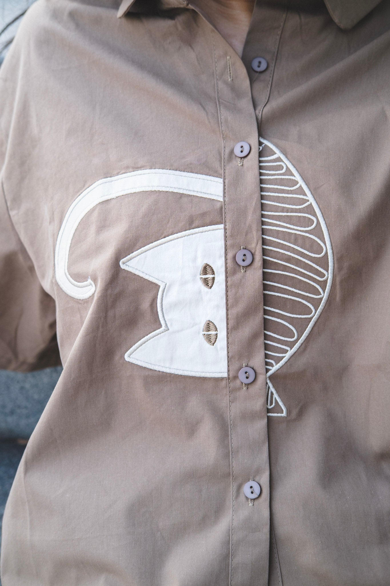 Close up shot of the half cat and half fish embroidery of the brown shiirt
