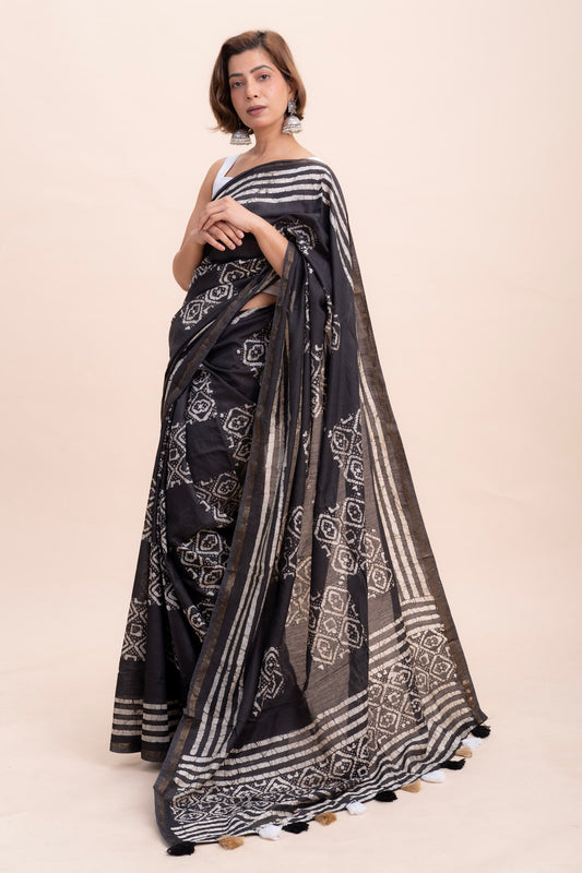 A woman in pure black cotton saree with a white geometric batik print and zari woven border featuring tassels.